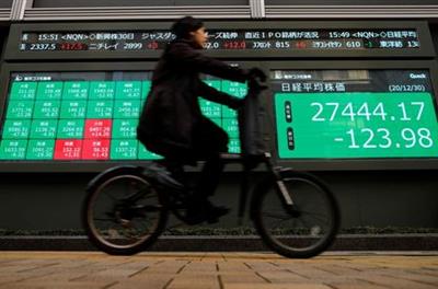 A man rides a bicycle past a screen displaying Nikkei share average and stock indexes outside a brokerage, amid the coronavirus disease (COVID-19) outbreak, in Tokyo, Japan December 30, 2020. REUTERS/Issei Kato