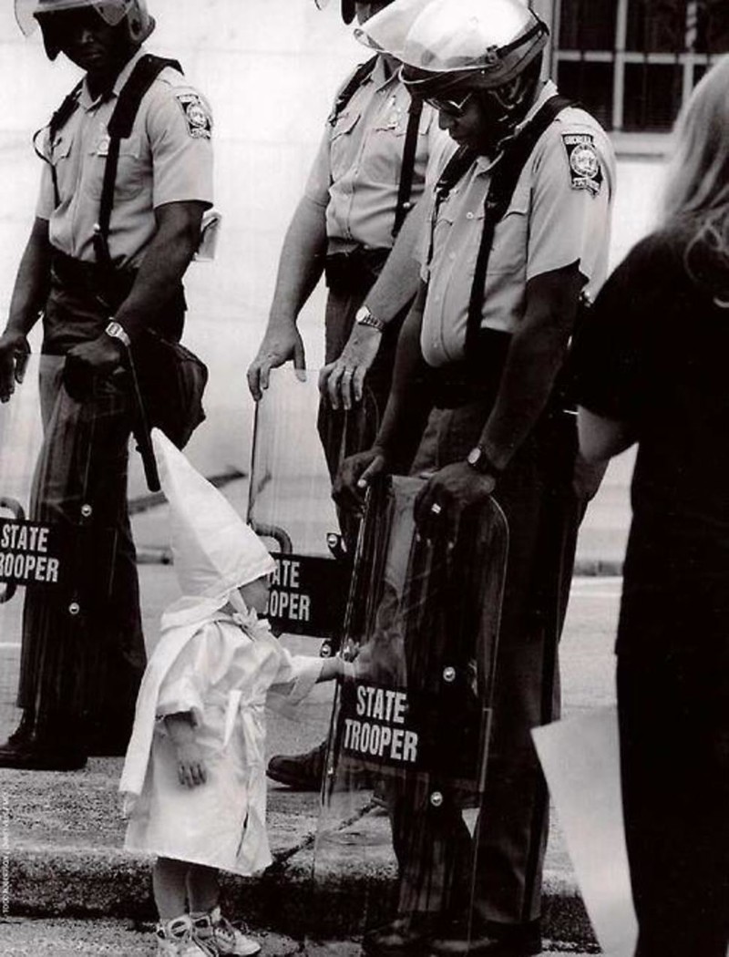 Ребенок члена организации Ку-клукс-клан во время демонстрации дотрагивается до своего отражения в полицейском щите, который держит полицейский-афроамериканец (1992 г.) подборка фото, хорошие фото, эмоции