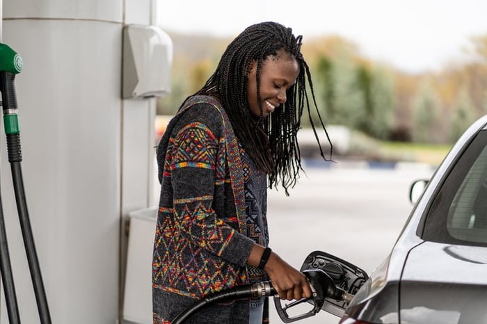 Person smiling while pumping fuel into vehicle's gas tank.