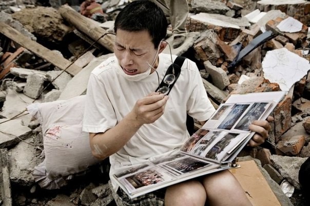 Парень смотрит семейный альбом, найденный в руинах своего дома после землетрясения в Сычуани история, события, фото