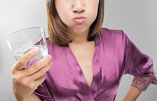 Woman rinsing and gargling while using mouthwash from a glass, During daily oral hygiene routine, Girl in a purple silk robe, Dental Healthcare Concepts