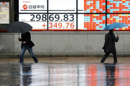Men holding umbrellas walk in front of an electric board showing Nikkei index at a brokerage in Tokyo, Japan February 15, 2021. REUTERS/Kim Kyung-Hoon