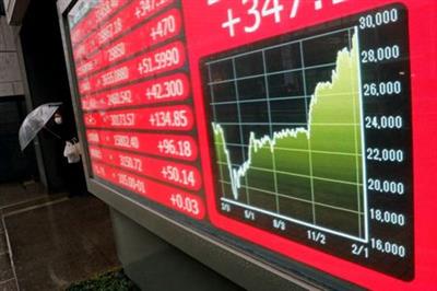 A woman holding an umbrella walks near an electric board showing Nikkei index at a brokerage in Tokyo, Japan February 15, 2021. REUTERS/Kim Kyung-Hoon