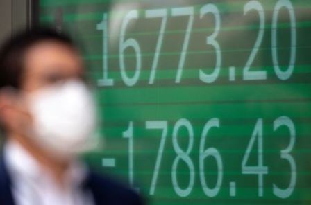 A man wearing a protective face mask, following an outbreak of coronavirus (COVID-19), walks past a screen showing the Nikkei index outside a brokerage in Tokyo, Japan, March 13, 2020. REUTERS/Athit Perawongmetha