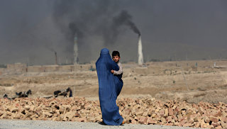Женщина с ребенком на руках идет мимо кирпичного завода на окраине Кабула, Афганистан, архивное фото